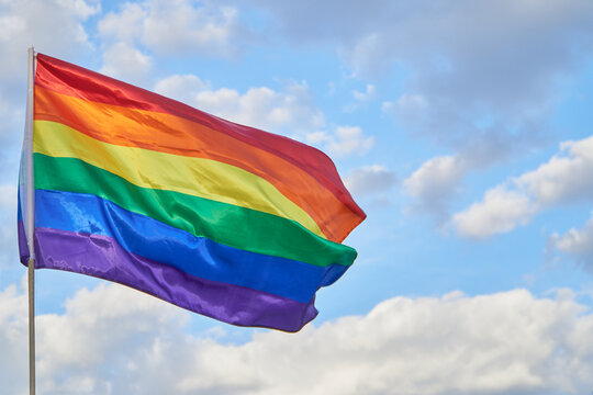 LGBTQ pride flag waving on blue sky with clouds