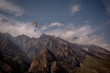Paragliding flight among rocky mountains and clouds. A sunny, spring day. Extreme, leisure, sports, hobbies. Cover, calendar, wallpaper, screensaver. Kabardino-Balkaria.