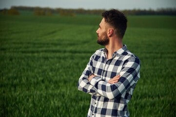 Standing with arms crossed. Handsome young man is on agricultural field