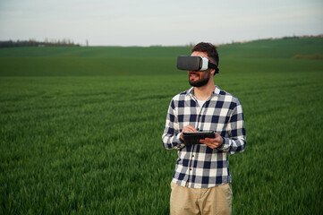 In virtual reality glasses. Handsome young man is on agricultural field