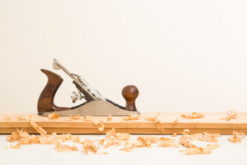 Manual jointer and shavings on old wooden plank on white table at light gray wall background. Closeup. Preparing material for repair work of home. Side view.