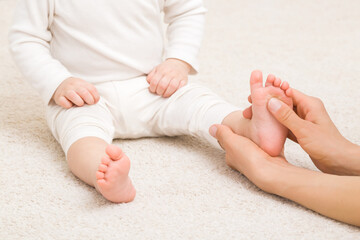 Masseur hand holding infant leg and massaging foot on carpet. Baby healthcare. Closeup. Front view. - 601047328