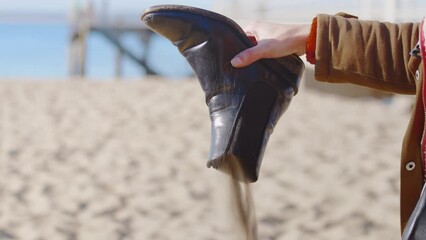 Female Tourist Shakes Sand Out Of Her Black Boots. Close up