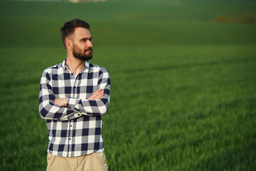 Standing with arms crossed. Handsome young man is on agricultural field