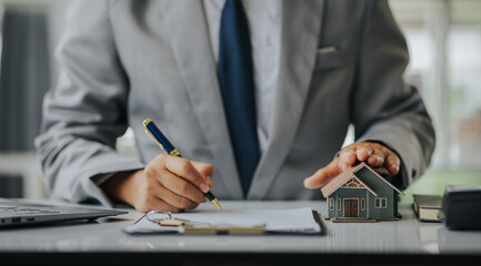 Businessman or real estate agent with house model laying down contract, having contract in place to...