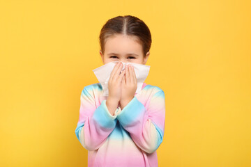 Girl blowing nose in tissue on orange background. Cold symptoms