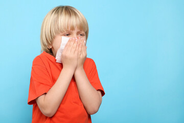 Boy blowing nose in tissue on light blue background, space for text. Cold symptoms