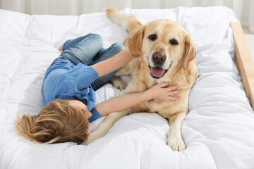 Cute little child with Golden Retriever on bed. Adorable pet