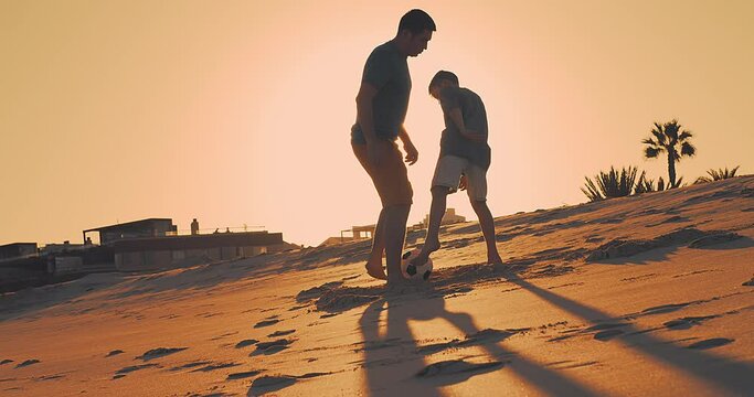Father and Son playing football on the beach, family fun outdoors players in soccer in dynamic action have fun playing football, summer day under sunlight. Togetherness Friendly concept
