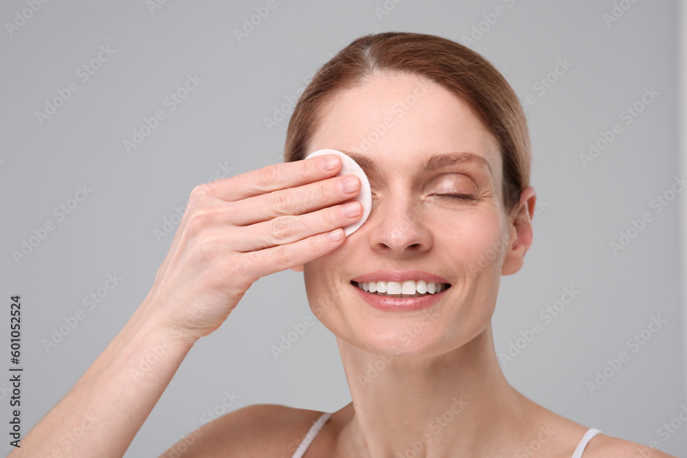 Wall mural Beautiful woman removing makeup with cotton pad on gray background