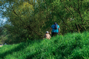 Adult father and teen son ride on a green hill against the background of green trees on a sunny spring day, trend photo, father and child, long shadow, sustainable environmentally friendly transport