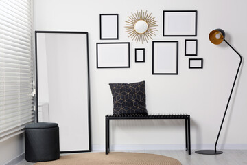 Stylish room interior with empty frames hanging on white wall and comfortable furniture