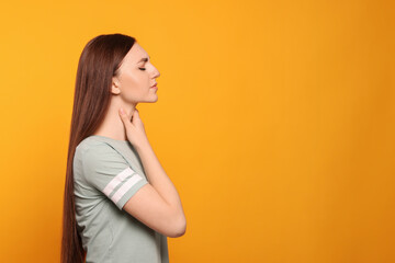 Young woman with sore throat on orange background