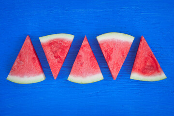 slices of watermelon in triangular shapes on a bright blue wooden surface - obrazy, fototapety, plakaty