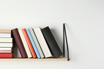 Wooden shelf with many hardcover books on white wall. Space for text