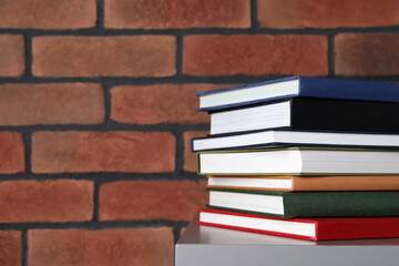 Many hardcover books on grey table near brick wall