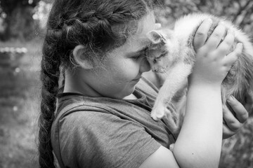 In the summer in the village, a little girl hugs a small homeless kitten. Black and white photo.