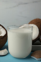 Glass of delicious vegan milk and coconuts on light blue wooden table