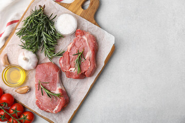 Fresh raw meat with rosemary, oil, tomatoes and spices on light grey table, flat lay. Space for text
