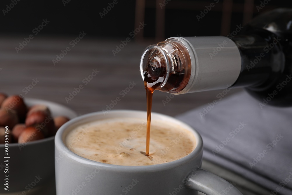 Canvas Prints Pouring delicious hazelnut syrup into cup with coffee at table, closeup