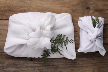 Furoshiki technique. Gifts packed in white fabric and thuja branches on wooden table, flat lay