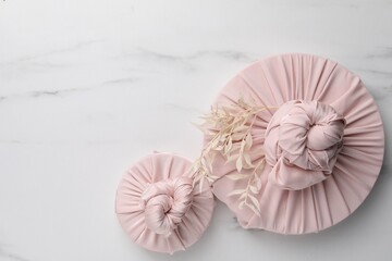 Furoshiki technique. Gifts packed in pink fabric and dried branches on white marble table, flat lay. Space for text