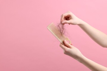 Woman untangling her lost hair from comb on pink background, closeup and space for text. Alopecia...