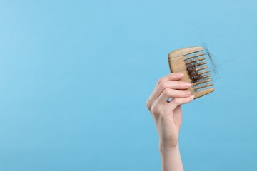 Woman holding comb with lost hair on light blue background, closeup and space for text. Alopecia...