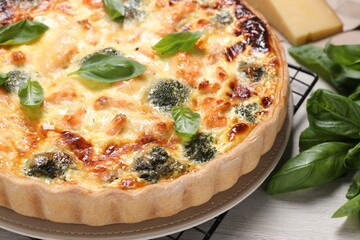 Delicious homemade quiche with salmon, broccoli and basil leaves on table, closeup