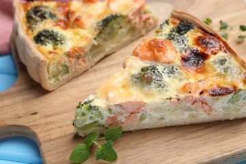 Pieces of delicious homemade quiche with salmon and broccoli on wooden board, closeup