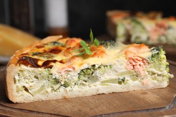 Piece of delicious homemade quiche with salmon and broccoli on wooden board, closeup