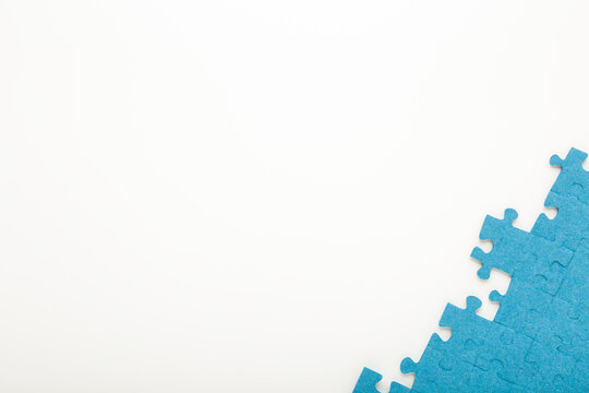 Unfinished blue puzzle pieces on white table background. Closeup. Empty place for text. Top down view.