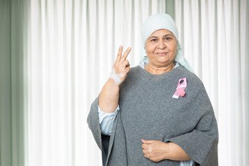 Portrait of indian senior woman cancer patient survivor standing with victory hand gesture at...