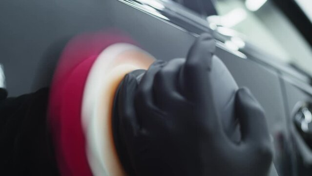 Closeup hands professional car washing worker using an electric-powered polishing machine to work on fender of beautiful black sportscar after washing and detailing the vehicle