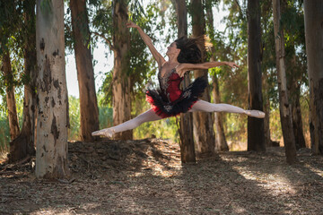 classical ballet dancer in a red, white and black dress in an autumn forest, performing a big acrobatic jump