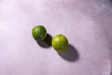 A pair of limes sit on a purple surface.