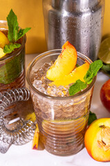 Iced peach tea, or peach lemonade with lime, mint,crushed ice and bar utensils 
on high-colored golden beige background 