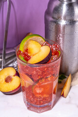 Iced plum tea, or plum lemonade with lime, mint,crushed ice and bar utensils 
on high-colored background 