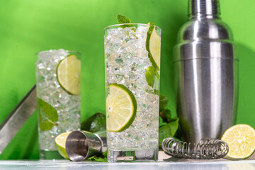 Classic summer cold mojito cocktail, lime lemonade with lime, mint,crushed ice and bar utensils on high-colored white green background