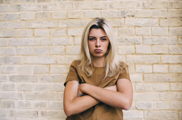 Discontent young woman standing near brick wall - obrazy, fototapety, plakaty