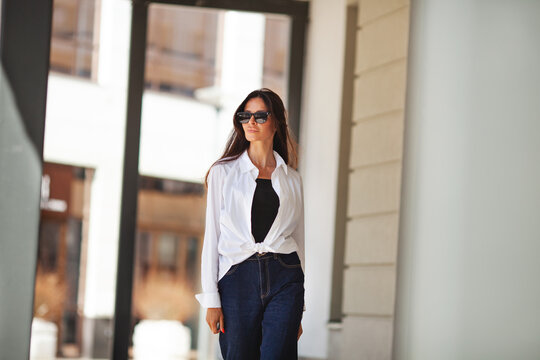 Portrait of fashionable business woman in white shirt walking outdoors. Stylish fashion model brunette with long hair