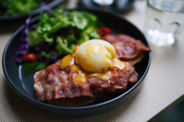 Western breakfast. Poached eggs on Hollandaise with pork bacon, bread and vegetable on the black ceramic plates