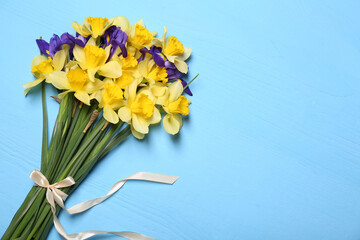 Bouquet of beautiful yellow daffodils and iris flowers on light blue wooden table, top view. Space for text