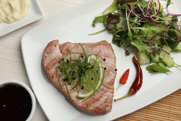 Delicious tuna steak served with salad and sauces on white wooden table, flat lay
