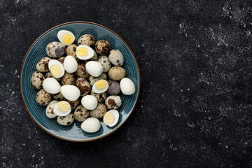 Obraz na płótnie Canvas Peeled and unpeeled hard boiled quail eggs in plate on black table, top view. Space for text