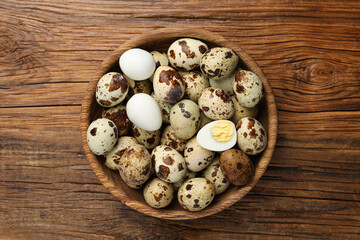 Unpeeled and peeled hard boiled quail eggs in bowl on wooden table, top view - obrazy, fototapety, plakaty