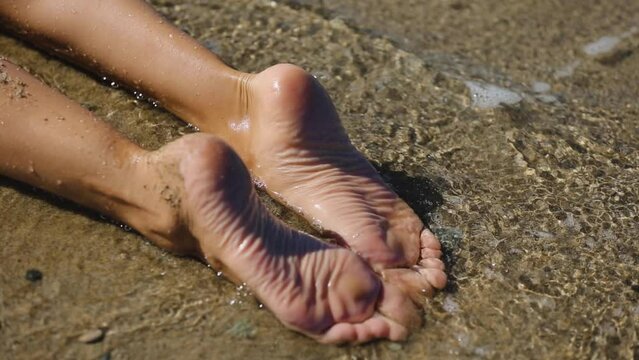 Female bare feet lie in the sea on a sandy beach. Close Up bare legs