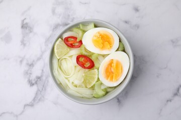Bowl of delicious rice noodle soup with celery and egg on white marble table, top view