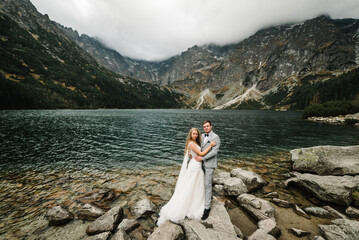 Romantic wedding couple in love standing on the stony shore of the Sea Eye lake in Poland. Scenic...