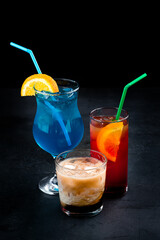 Alcoholic cocktails Tequila Sunrise, Blue Lagoon and White Russian on a dark background.